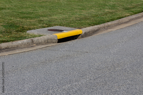 Residential street curb with drain painted yellow, green grass and asphalt copy space, horizontal aspect photo