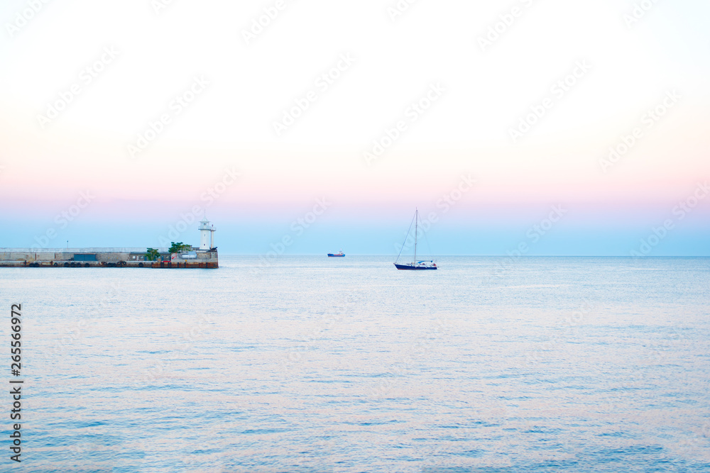Obraz premium Sea sunset in summer in the evening with natural light Sea sunset, yachts in the sea near the lighthouse on a summer day in the background of beautiful colors in the sky 