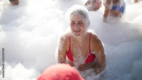 4k slow motion video of beautiful young woman having fun and dancing in soap foam on the beach. Girl relaxing on the outdoor party photo