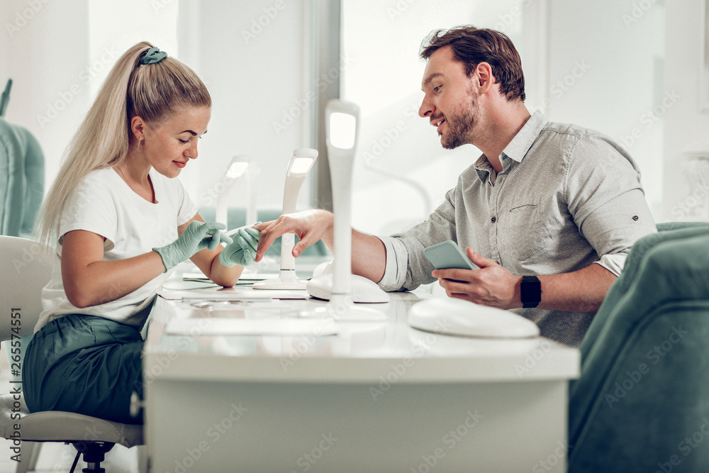 Obraz premium Curious dark-haired man in light shirt observing work of pretty nail master