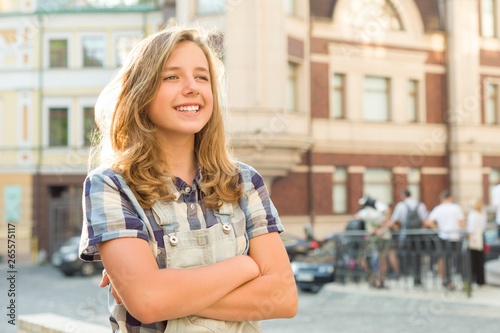 Outdoor portrait of smiling teenager girl 12, 13 years old on city street, girl with folded hands, copy space