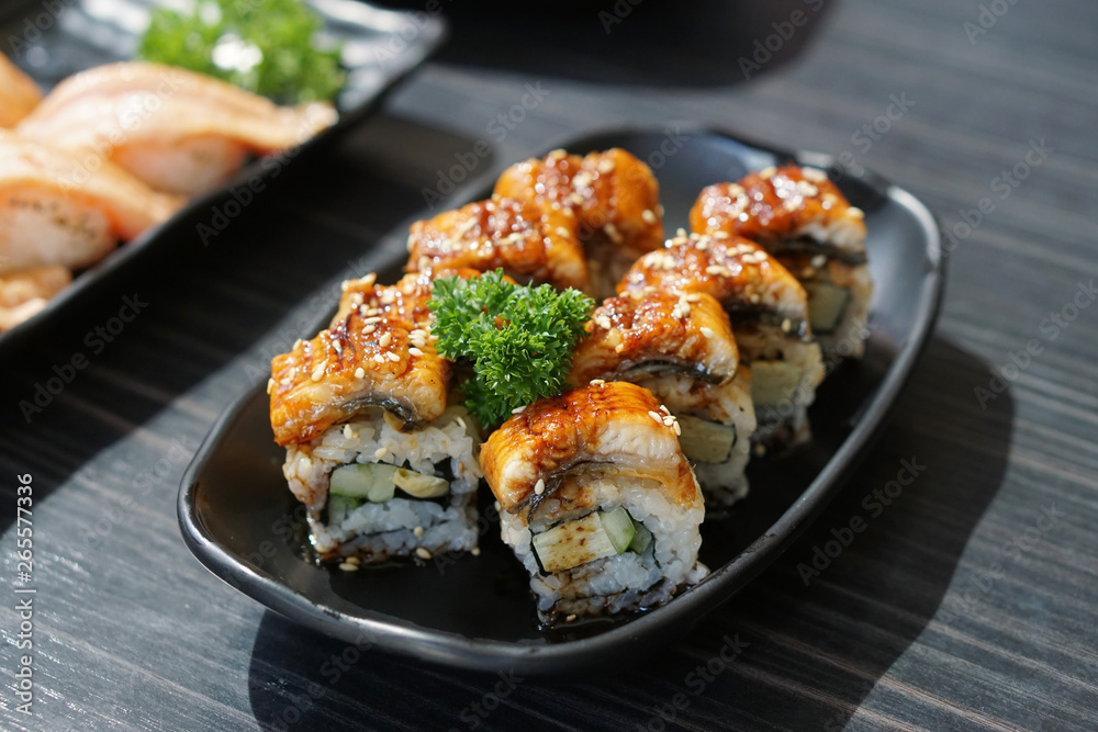 Unagi sushi roll - A plate of steamed rice topped with grilled freshwater eel and sweet sauce on wooden table, Traditional Japanese Food. Unagi sushi roll - A plate of steamed rice topped with grilled freshwater eel and sweet sauce on wooden table, Traditional Japanese Food.