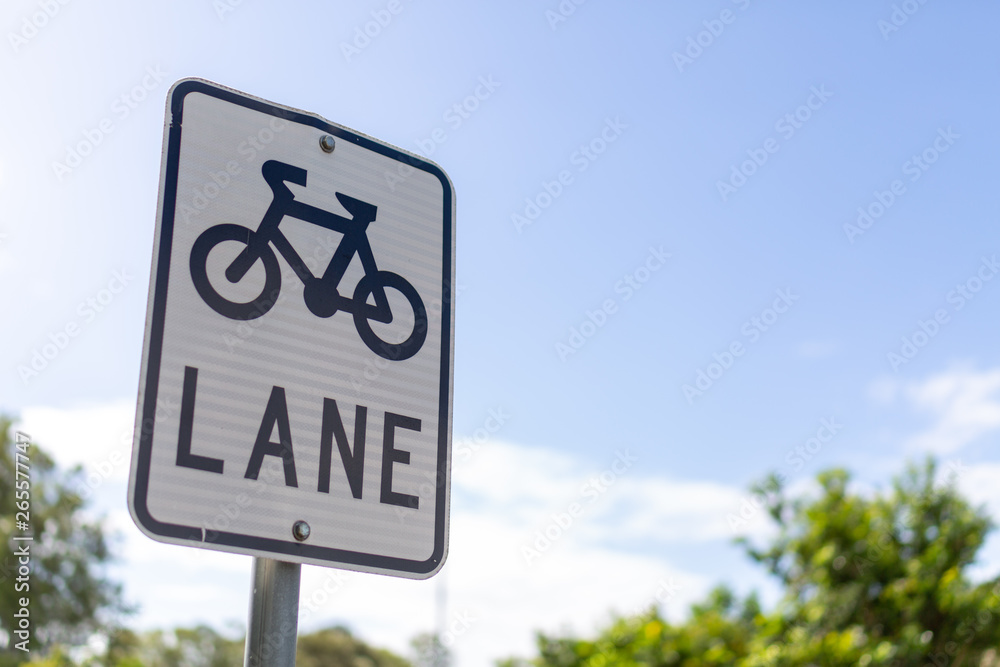 A bicycle lane sign attached to a pole with blue sky green and bushes in the background. A bicycle lane sign attached to a pole with blue sky green and bushes in the background.