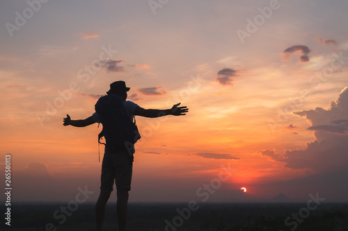 Traveler with backpack watching amazing sunset. Silhouette of the young man on the mountain top