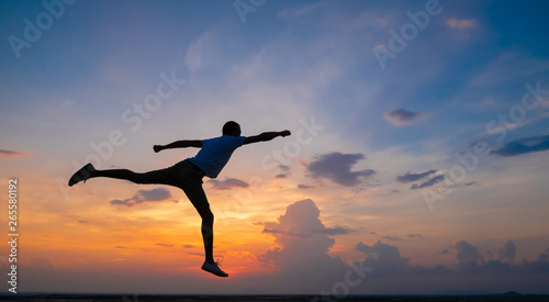 Happy man jumping for joy on the peak of the mountain, cliff at sunset. Success, winner, happiness
