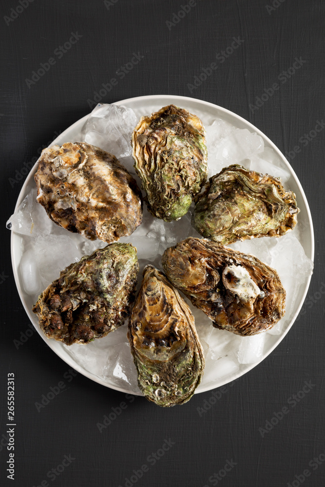 Fresh oysters on ice on gray plate over black surface, top view. Flat lay, overhead, from above. Close-up. Fresh oysters on ice on gray plate over black surface, top view. Flat lay, overhead, from above. Close-up.