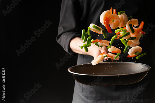 Seafood, Professional cook prepares shrimps with sprigg beans. Cooking seafood, healthy vegetarian food and food on a dark background. Horizontal view. Eastern kitchen