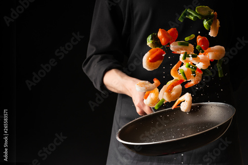 Fototapeta Naklejka Na Ścianę i Meble -  Seafood, Professional cook prepares shrimps with vegetables. Frost in the air, Cooking seafood, healthy vegetarian food and food on a dark background. Horizontal view. Eastern kitchen, banner