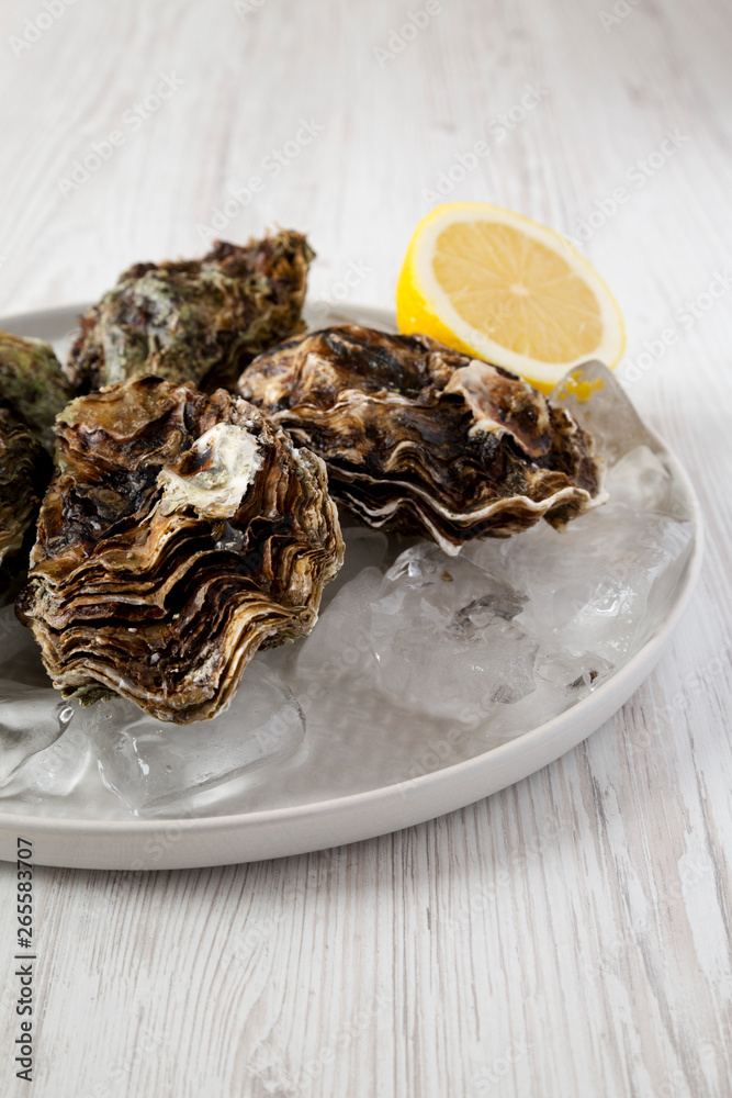 Fresh oysters on ice on a plate over white wooden surface, side view. Close-up. Fresh oysters on ice on a plate over white wooden surface, side view. Close-up.