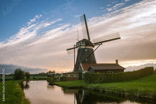 Classic scene of a dutch windmill and house near a canal with a great sky as background. © Menyhert