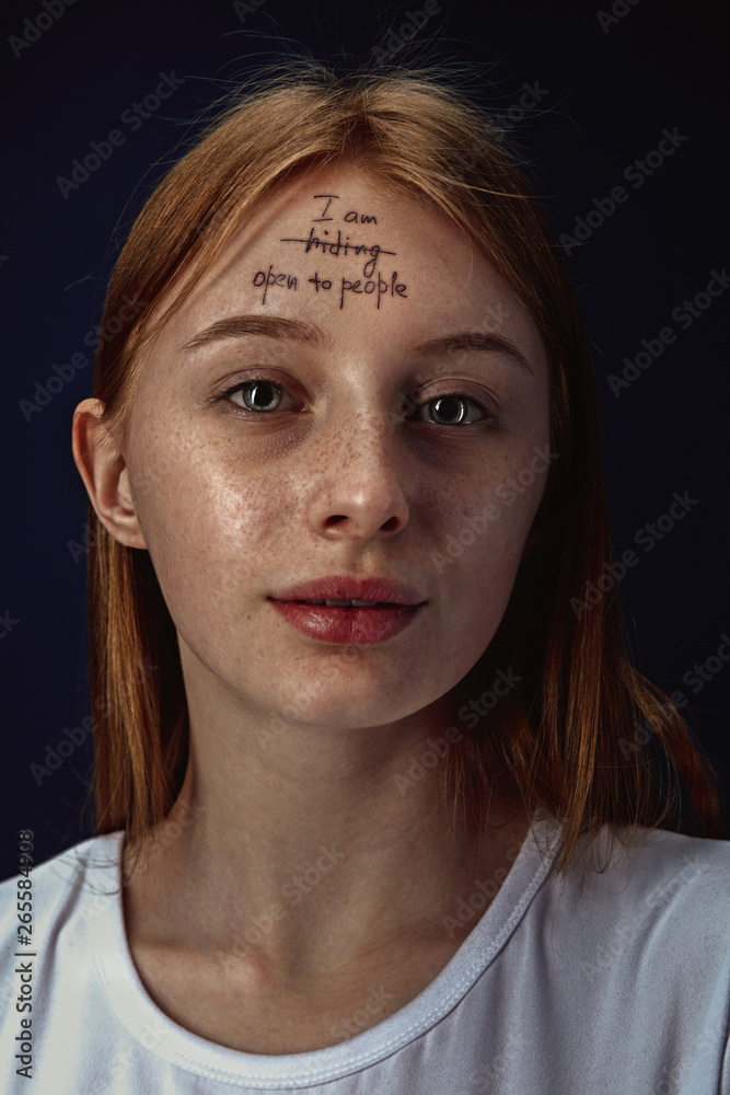 Portrait of young woman overcoming mental health problems. Tattoo on the forehead with the words I'm hiding-open to people. Concept of psycological rehabilitation, return to healthy lifestyle.