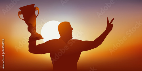 Concept du succès avec un sportif qui savoure sa victoire en brandissant le trophée gagné lors d’une compétition sportive et en faisant le signe de la victoire.