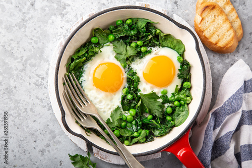 Healthy breakfast. fried eggs with kale, spinach and green peas in red skillet