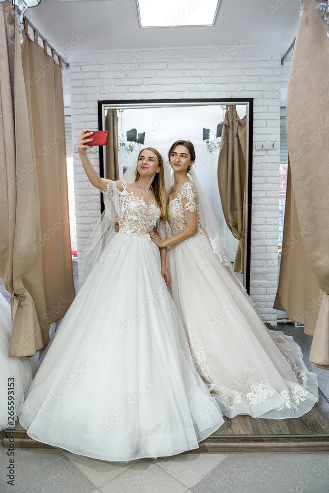 Friends in wedding dresses making selfie in salon