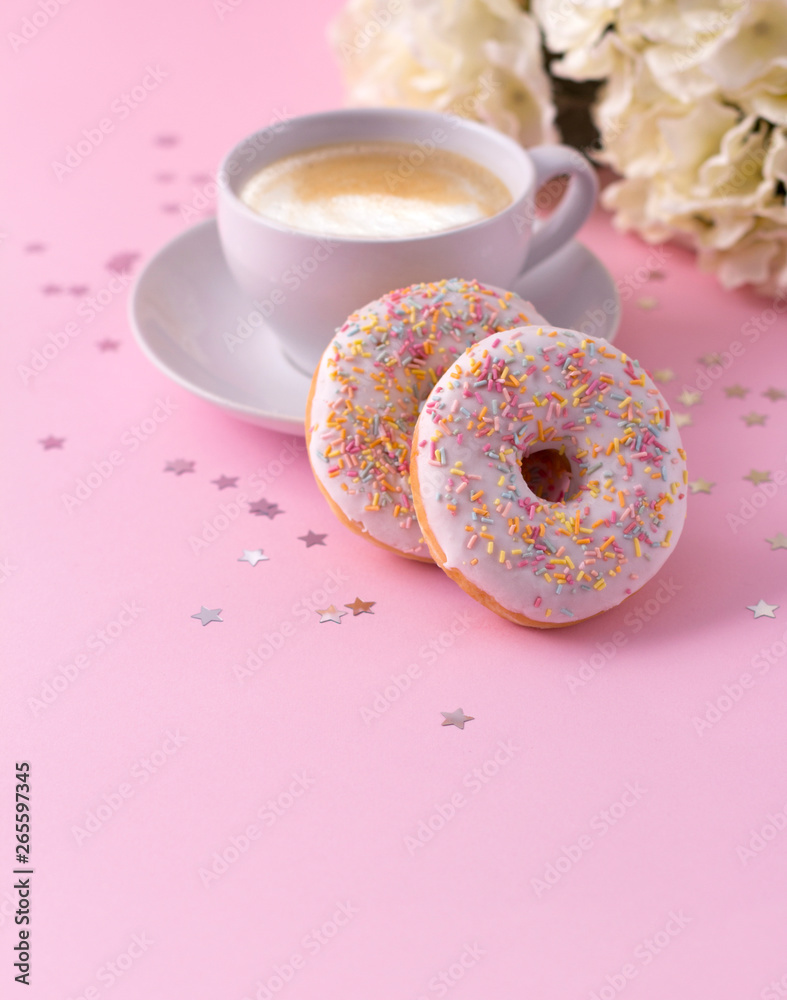 Mug of hot cappuccino and two donuts with flowers on a pink background. Mug of hot cappuccino and two donuts with flowers on a pink background.