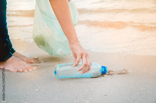 Woman's hand picking up plastic bottle garbage by the beach. Volunteering concept.