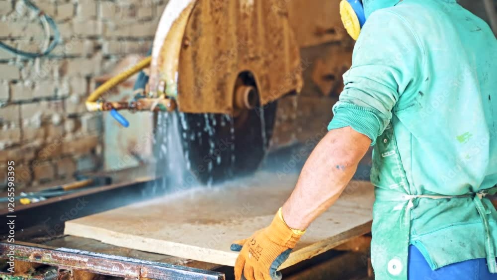 Man worker controls the factory CNC machine. Automated machine for cutting stone slab. Running water while sawing the stove indoors. Man worker controls the factory CNC machine. Automated machine for cutting stone slab. Running water while sawing the stove indoors.
