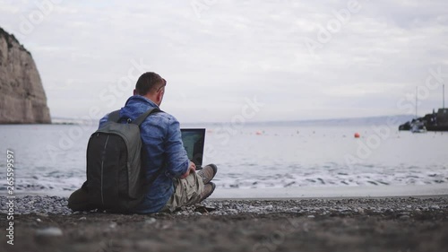 man, guy the photographer working with a laptop on the beach, backpack, concept of find information at travel to foregin country, communication, mountains on background photo