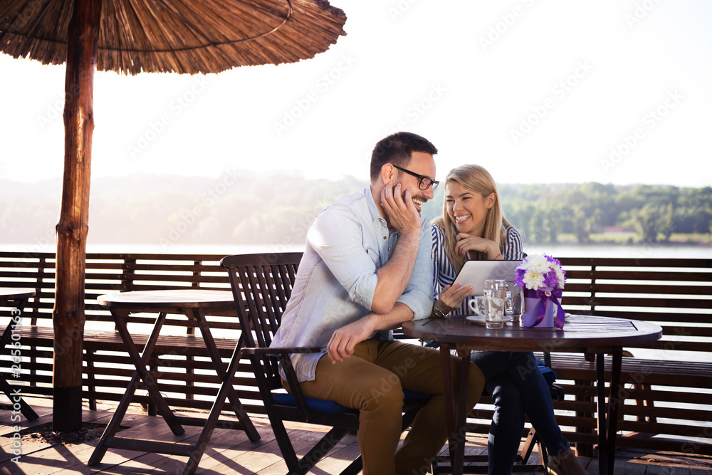 Bearded young man with glasses sits next to his girlfriend blond in a restaurant by the river.