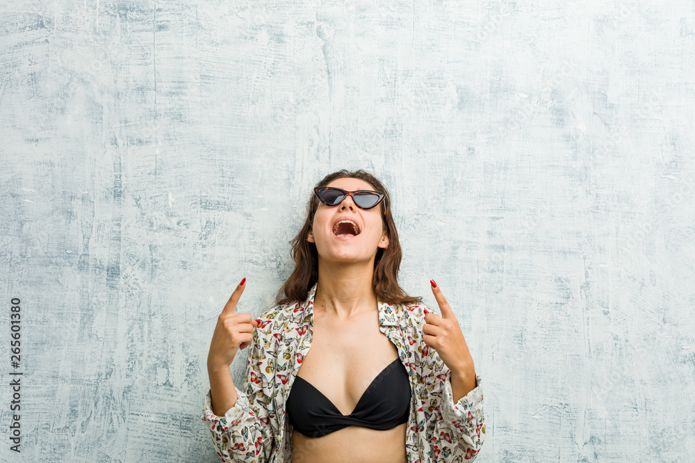 Fototapeta premium Young european woman wearing bikini indicates with both fore fingers up showing a blank space.