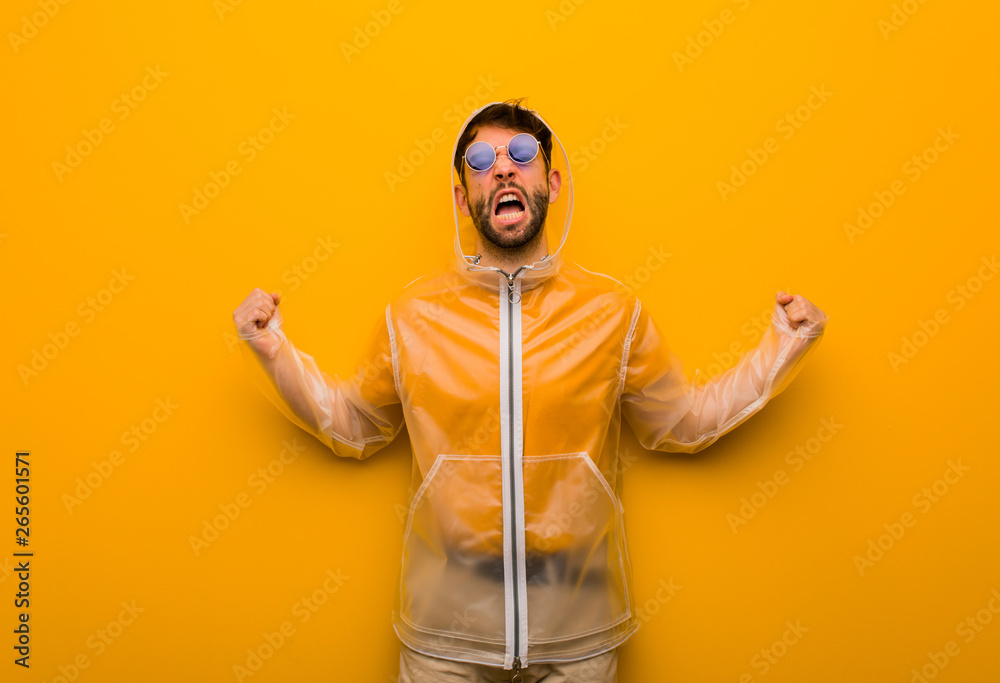 Young man wearing a rain coat screaming very angry and aggressive