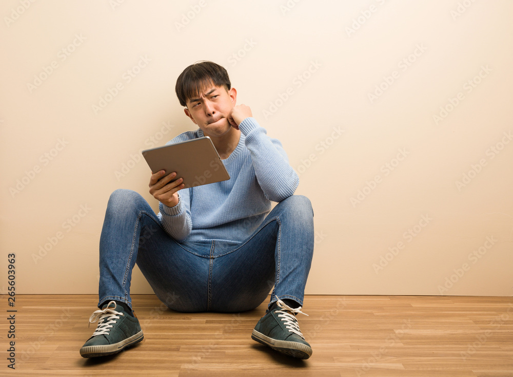 Young chinese man sitting using his tablet thinking about an idea