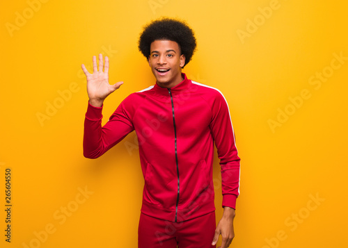 Young sport black man over an orange wall showing number five