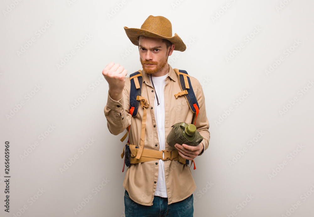 Young redhead explorer man showing fist to front, angry expression. He is holding a canteen. Young redhead explorer man showing fist to front, angry expression. He is holding a canteen.