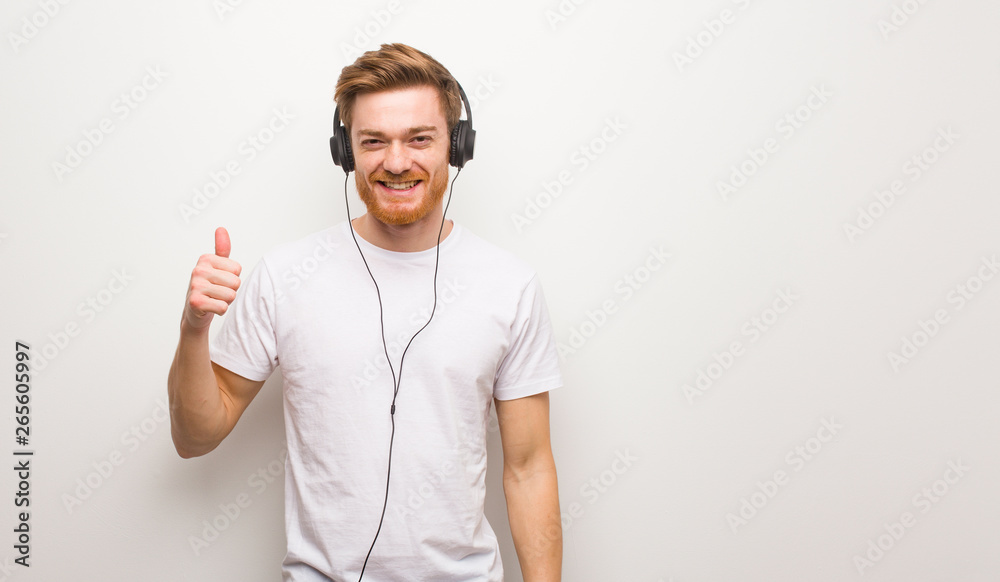 Young redhead man smiling and raising thumb up. Listening to music with headphones. Young redhead man smiling and raising thumb up. Listening to music with headphones.