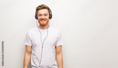 Young redhead man cheerful with a big smile. Listening to music with headphones.