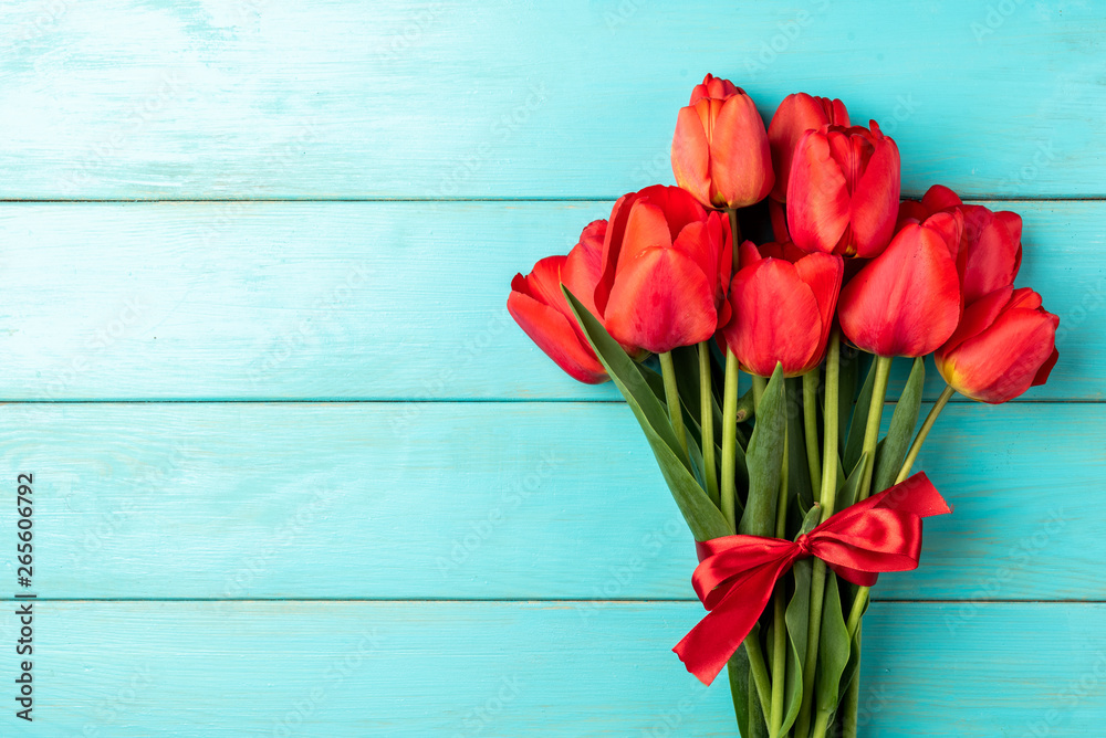 Red tulips with red ribbon on blue wooden background. 