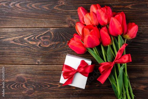 Red tulips with red ribbon and gift box on wooden background.