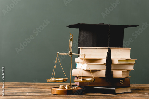 books, academic cap and scales on wooden surface isolated on grey