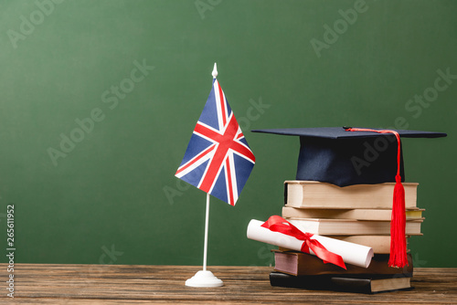 Books, academic cap, diploma and british flag on wooden surface isolated on green