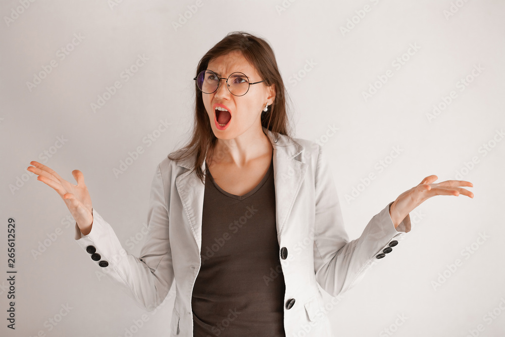 Excited screaming young woman in glasses standing isolated over light gray background. Looking at camera. - obrazy, fototapety, plakaty 