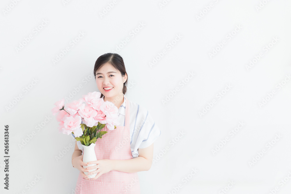 White Thai woman, long hair, wearing a casual dress and pink apron, holding a vase of flowers on a white wall in the morning in Thailand with Copy Space