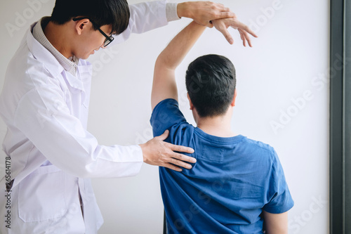Doctor physiotherapist assisting a male patient while giving exercising treatment massaging the shoulder of patient in a physio room, rehabilitation physiotherapy concept photo