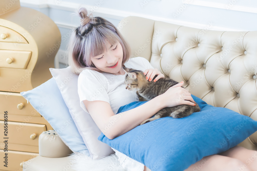 Beautiful young Asian Thai woman was lying on the sofa with his cat happily and stroking the cat's head with love in the living room in the morning in Bangkok, Thailand. Beautiful young Asian Thai woman was lying on the sofa with his cat happily and stroking the cat's head with love in the living room in the morning in Bangkok, Thailand.