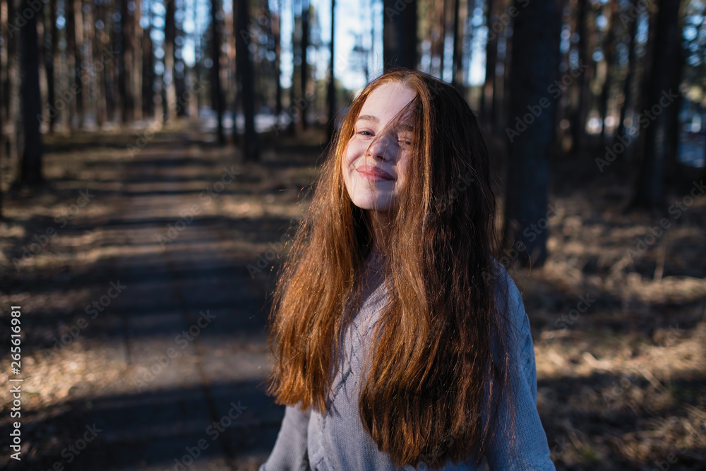 Cute schoolgirl with long red hair posing for the camera in a pine park in the summer. Cute schoolgirl with long red hair posing for the camera in a pine park in the summer.