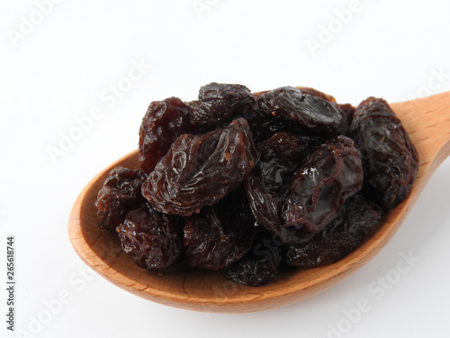 High angle view of raisins on wooden spoon isolated on white background. A raisin is a dried grape Dry food. It tastes sweet and delicious. Texture detail of raisin surface. Food concept.