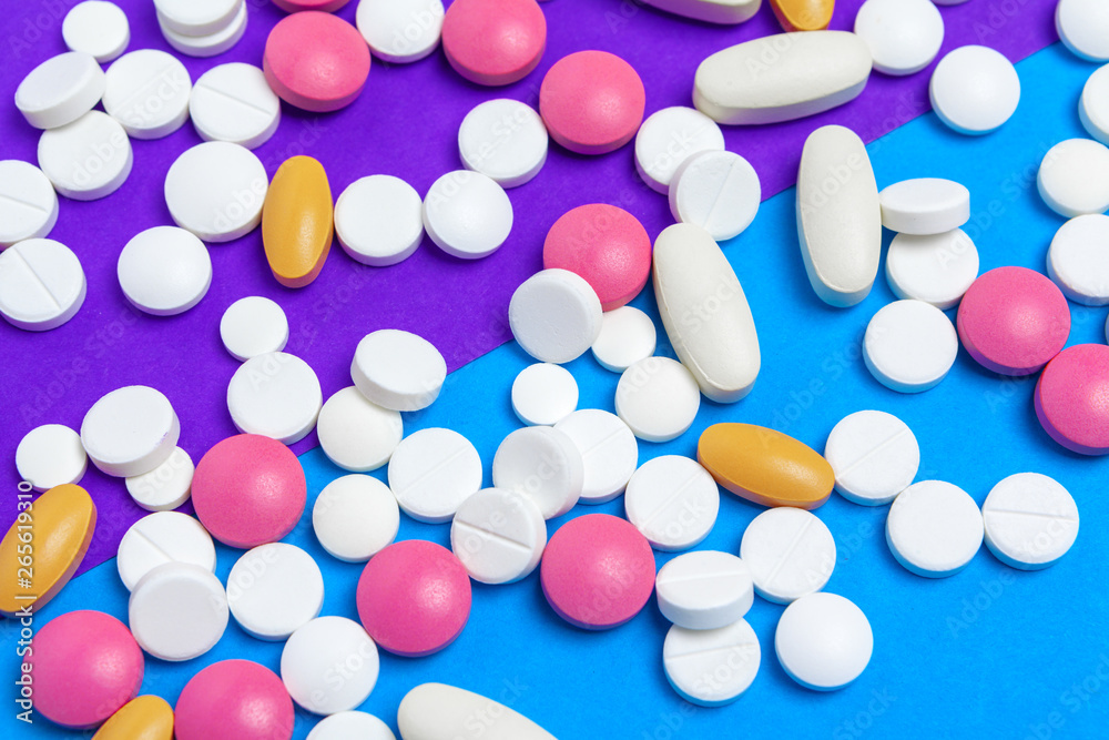 A pile of multicolored pills on blue background. Top view. A pile of multicolored pills on blue background. Top view.