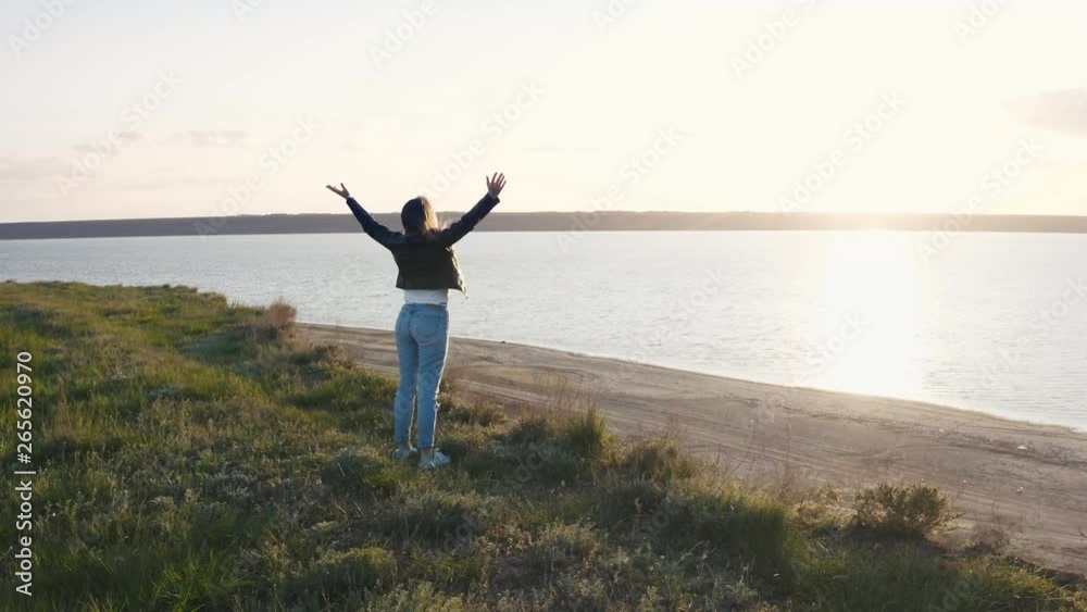 Tracking aerial shot of young woman enjoying sunset in field near the cliff during beatiful sunset Tracking aerial shot of young woman enjoying sunset in field near the cliff during beatiful sunset