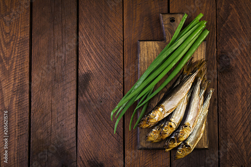 Smoked sprat and green onion  on a cutting board on a wooden background. Smoked fish. Top view