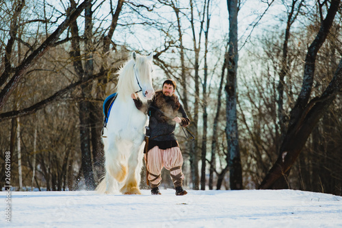 Man in suit of ancient warrior walking with the big white horse