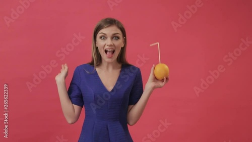 Beautiful girl in a dress drinking orange juice with a cocktail straw and dancing. Studio, purple background photo