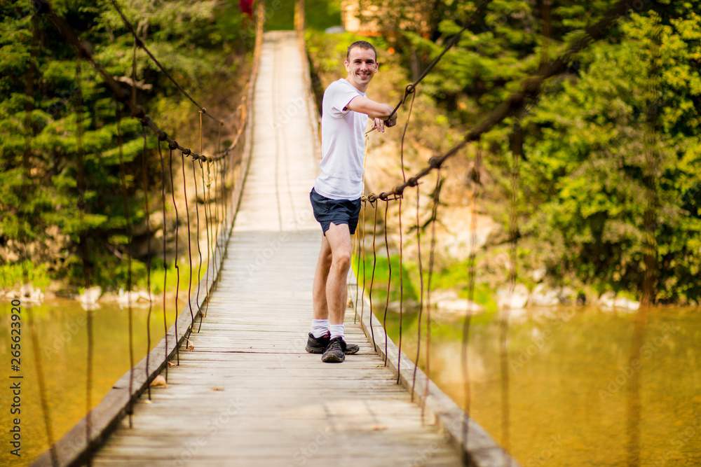 Young happy man on bridge over river in autumn nature with moun