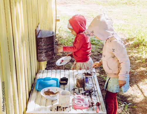 Canvastavla Two young girls sisters play outdoors in so called mud kitchen, where you can make fake food, play with sand, dirt, water, plants and make a mess it develops imagination and exploration