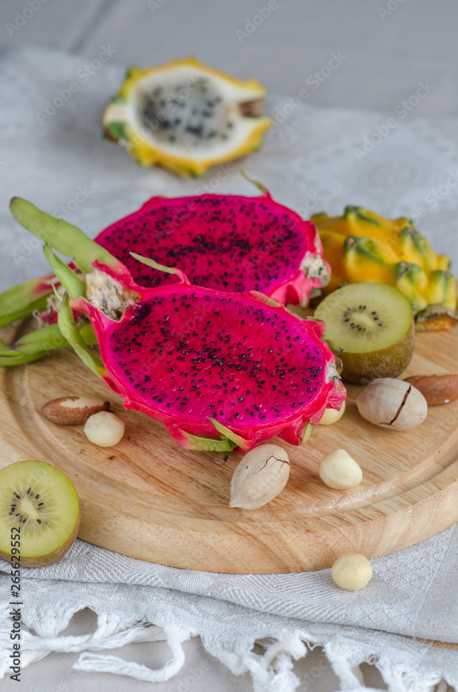 Assortment dragon fruit - yellow and red pitahaya, yellow kiwi and nuts on a wooden tray