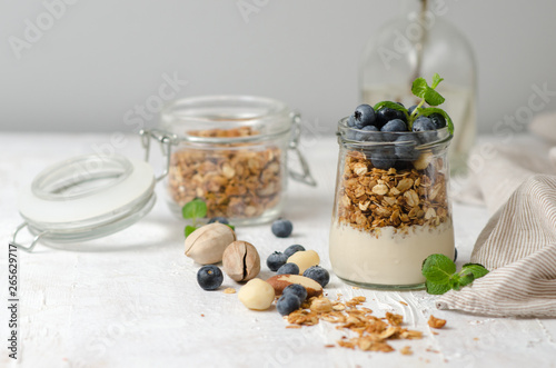 Healthy breakfast - glass jars of granola with fresh blueberries, yogurt, nuts and mint. Granola on a light background, space for text.