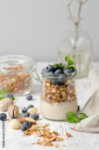 Healthy breakfast - glass jars of granola with fresh blueberries, yogurt, nuts and mint. Granola on a light background, space for text.